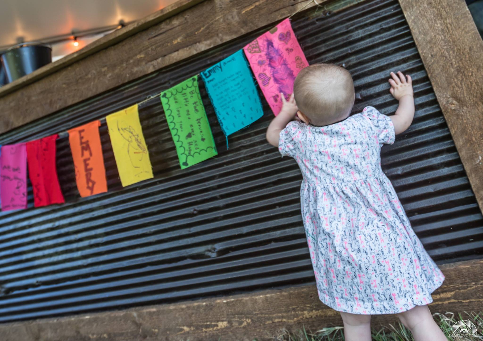 Baby Emmy reaching toward colorful prayer flags on a corrugated wall