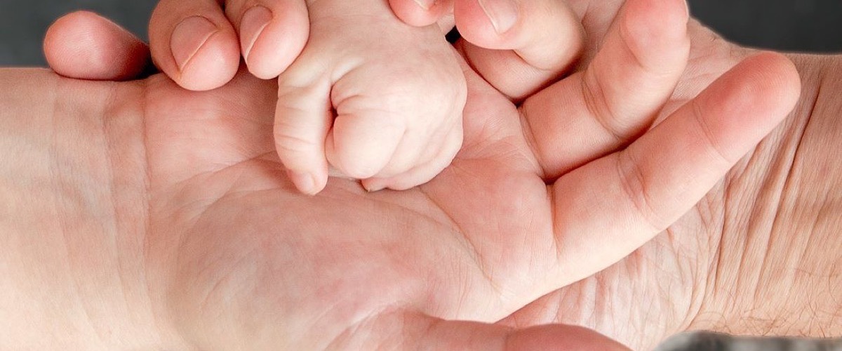 A parent's hands cradling a small child's hand